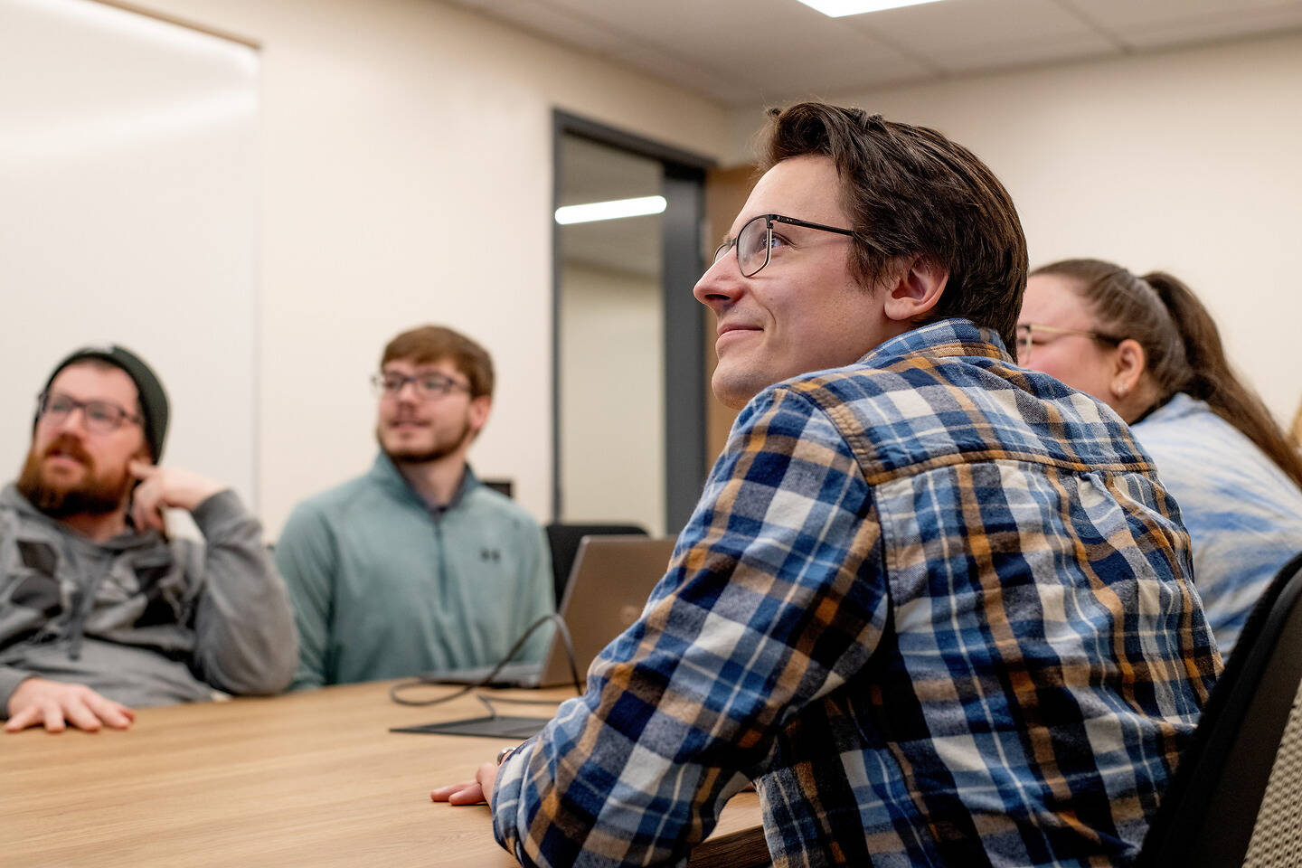A group of people are seated around a table in a meeting room, attentively listening and engaged in discussion.